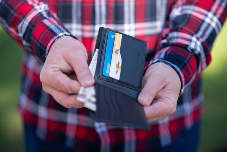 Ein Mann hat sein Portemonnaie mit Bargeld und Karten in der Hand und ist gerade dabei, einen Geldschein herauszuziehen.